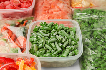 Containers and plastic bags with frozen vegetables as background