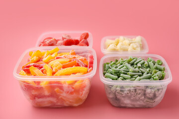 Plastic containers with frozen vegetables on color background