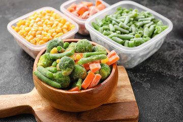 Wooden bowl and containers with frozen vegetables on dark background