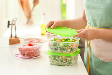 Woman holding plastic containers with frozen vegetables in kitchen