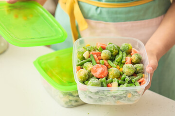 Woman holding plastic container with frozen vegetables in kitchen