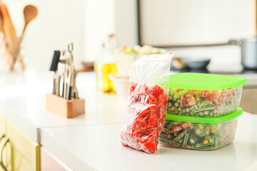 Plastic containers and bag with frozen vegetables on table