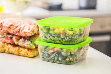 Plastic containers and bags with frozen vegetables on table