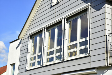 Hellgrau lasierte Holzfassade mit Giebeldach und Fenstern