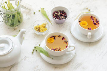 Herbs, teapot and cups with floral tea on light background