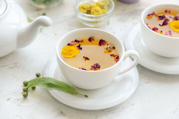 Herbs, teapot and cups with floral tea on light background