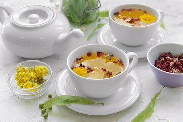Herbs, teapot and cups with floral tea on light background