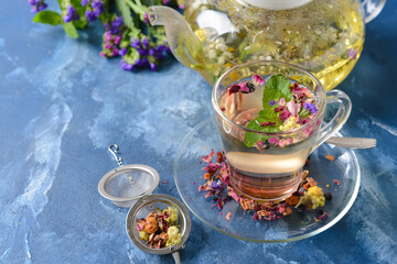 Teapot and cup with floral tea on color background