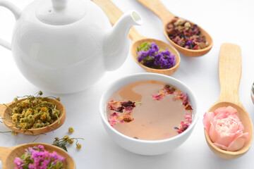 Dry flowers in spoons, teapot and cup with floral tea on light background