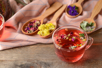 Cup of floral tea and spoons with dry flowers on wooden background