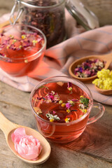 Cup of floral tea and spoons with dry flowers on wooden background