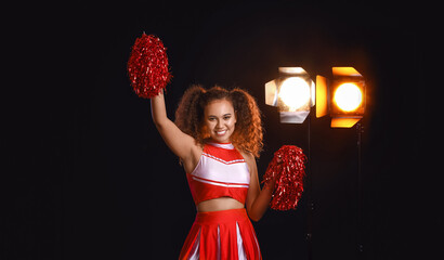 Beautiful young cheerleader on dark background