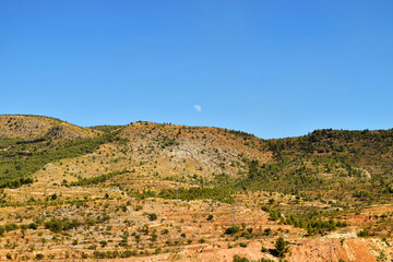Fototapeta na wymiar Mountainous landscape with the crescent moon appearing behind the mountains on a summer afternoon