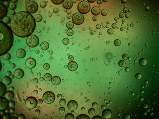 Makroaufnahme von Öltropfen in Wasser mit grün-orangenem Hintergrund.