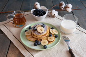 pancakes with berries and bananas on a plate, morning breakfast with tea and milk