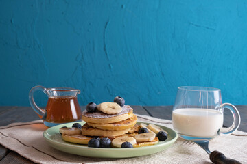 fresh pancakes with berries, honey and sliced bananas on a plate, morning breakfast with milk