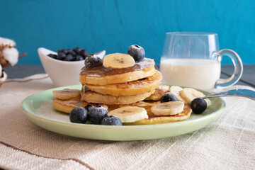 freshly baked pancakes, honey flows down them, with berries and chopped bananas on a plate, next to there is milk in a glass