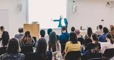 Speaker Giving a Talk at Business Meeting. Audience in the conference hall. Business and Entrepreneurship. Focus on unrecognizable people from rear.