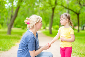 Little girl with syndrome down talks with her mother in a summer park