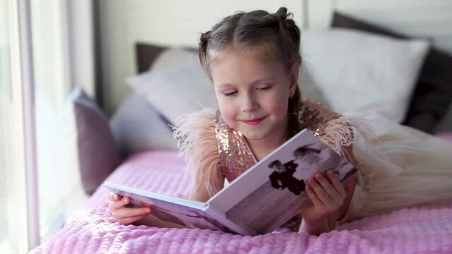 A little beautiful girl lies on the bed and looks at her parent is wedding photo album. Photo printing.