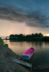 Storm arcus shaft and cumulonimbus cloud with heavy rain or summer shower, severe weather and sun glow behind rain. Landscape with Sava river with moored boat next to wooden dock during stormy evening
