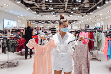 Young woman shopping apparels in clothing boutique with protective face mask