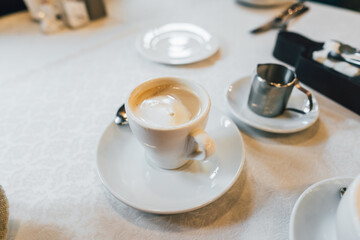 Small white cup of cappuccino stands on the table