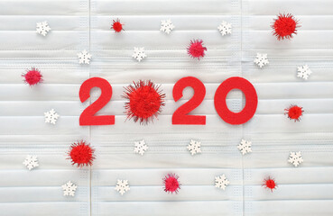 Red felt numbers 2020 on light blue medical masks background. First zero is fluffy pompon as a corona virus. Wooden white snowflakes and red pompons around. Results of the year.