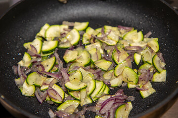 A frying pan in a kitchen frying onions and cucumber slices