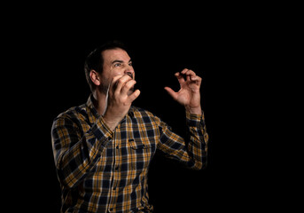 Attractive bearded man in a yellow plaid shirt posing pissed off with raised hands isolated on black background