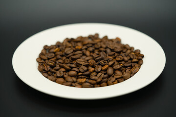 a white plate full of aromatic coffee beans against a dark background