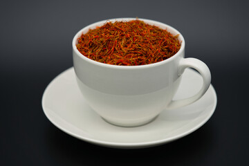 A white cup filled with dried saffron against a dark background