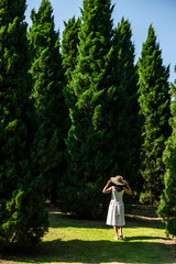 Back view adult woman in white dress with hands holding hat walking in a park