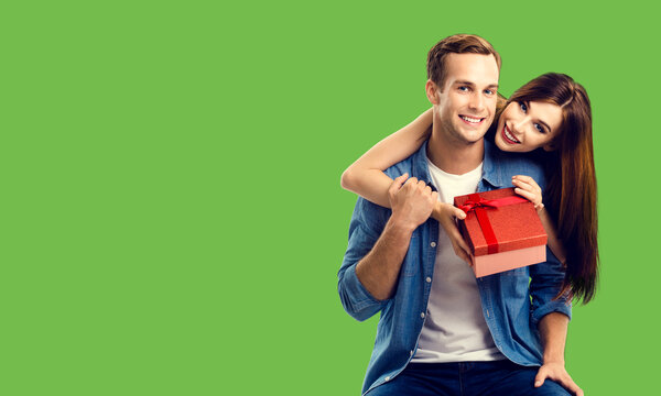 Love, relationship, dating, flirting, lovers concept - happy smiling amorous couple opening gift box. Green color background. Copy space.