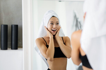 Woman in the bathroom with a towel on her head in front of a mirror.