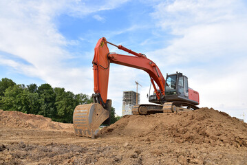 Excavator during excavation aond road construction works at construction site on sunset background. Backhoe on foundation work in sand pit.Tower crane on constructing new building