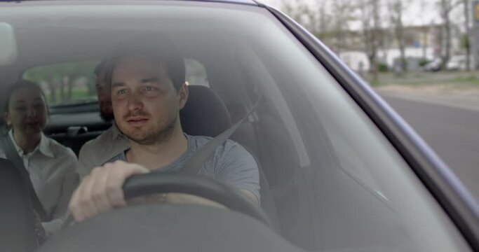 Concentrated young driver in the city road female and male client in back seat. View through front car window.