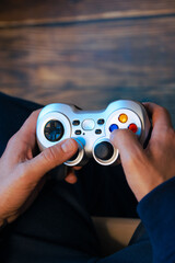 Close-up of a man's hands holding a video game controller with a screen in the background. Gamer and e-sports concept. Vertical photography and copy space.