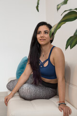 beautiful young woman doing stretching exercises on a white sofa with colorful cushions inside her...