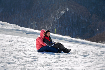 A woman and a young man on a snow sled running on a slope.