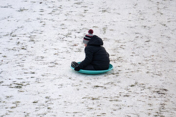 Fototapeta na wymiar unknown boy on a sled going down a snowy hill