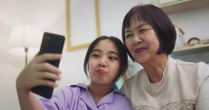 Asian grandmother and granddaughter video call at home. Happy senior and child using mobile phone video call talking with dad and mom sitting in living room at home.