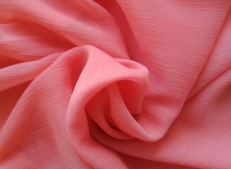 Coral color silk fabric slightly folded in a smooth spiral. Good for fresh texture, background or texture.