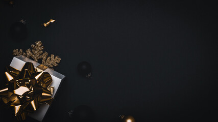 Xmas decoration. White gift with golden bow, gold balls and sparkling lights garland in Christmas decoration on dark background for greeting card. Flat lay, top view, copy space.