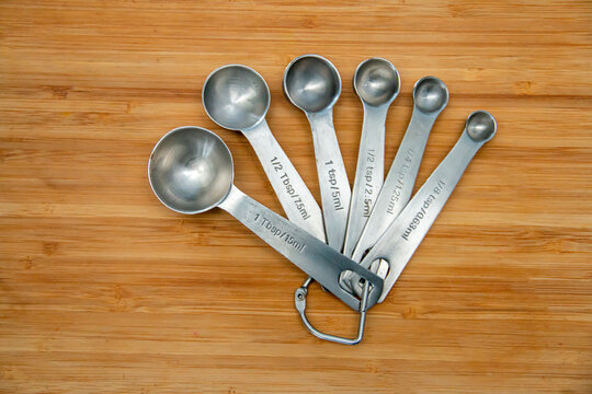 Silver measuring spoons on a wooden cutting board