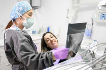 Female dentist pointing at patient's X-ray image in dental office. High quality photo