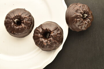 Three sweet chocolate marshmallows on a white plate, close-up, on a slate board.