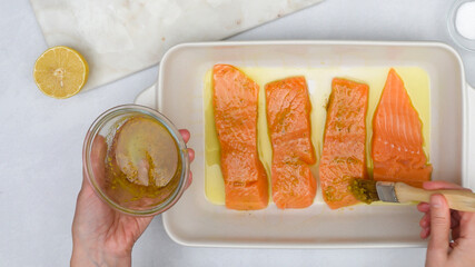 Baked salmon fillet recipe. Chef topping fish slices with marinade, close up view from above