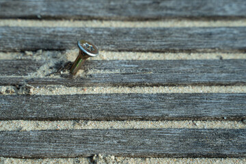 An iron nail sticks out of a board in the sand