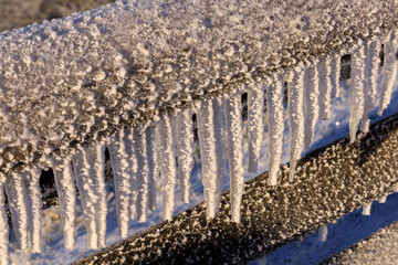 Closeup of icicles hanging from split rail fence in sunlight